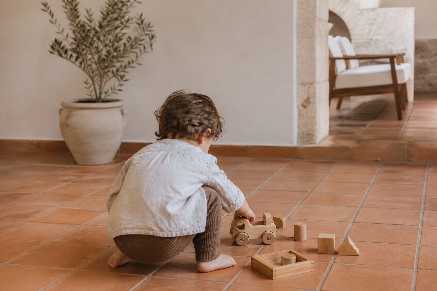 Terracotta zeminde ahşap oyuncaklarla oynayan iki yaşında çocuk